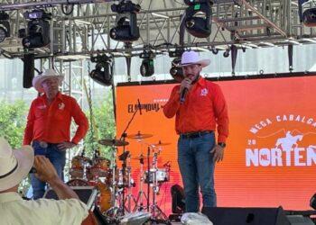 Two Men in Orange Shirts and White Cowboy Hats Sing on Stage with a Drum Kit; Orange Backdrop Reads 'norteÑa' and 'mega Cabalgata'. - Regios En México