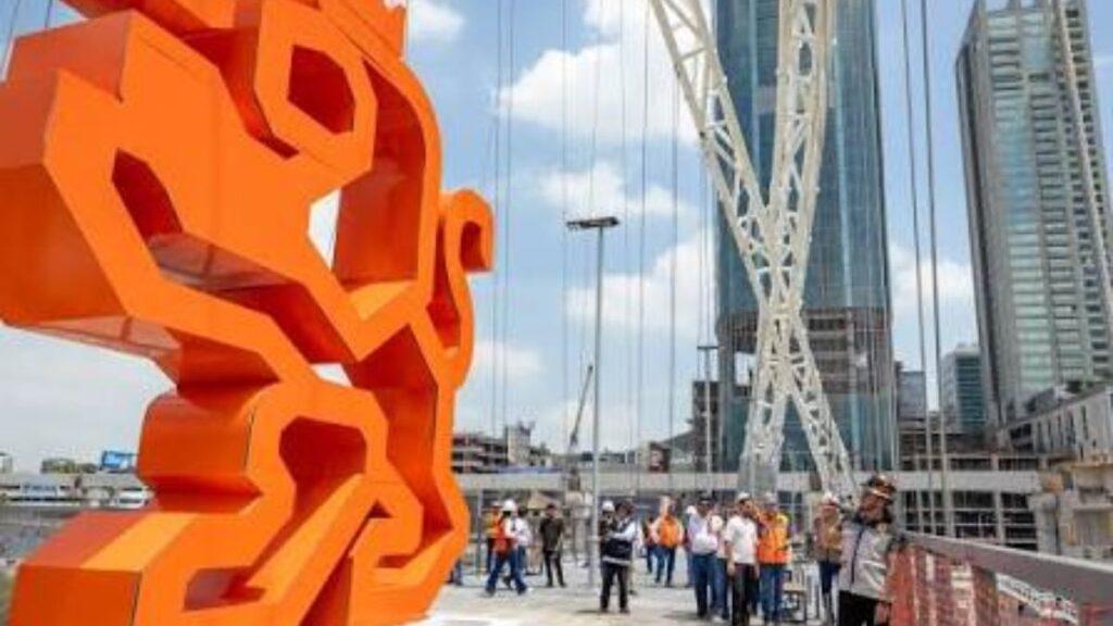 Samuel-garcia-totems-naranjas - Regios En México Large Orange Abstract Sculpture on a Pedestrian Bridge with People Observing and a City Skyline in the Background. - Regios En México